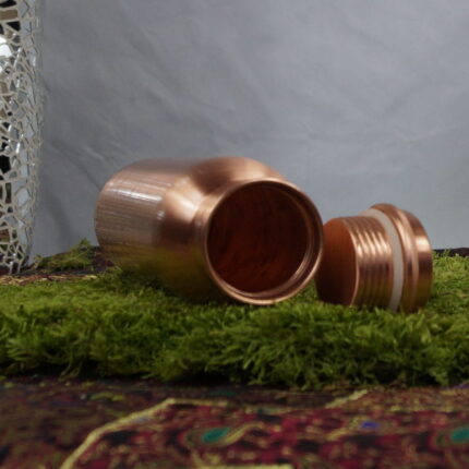 Die 'Copper Serenity Elegance' - eine Kupferflasche, die mehr ist als nur ein Gefäß. Mit ihrer erhabenen Höhe von 27,5 cm und der matten satinierten Politur strahlt sie zeitlose Eleganz aus. Die Oberfläche, empfindlich und doch charmant, erzählt Geschichten von jeder Begegnung mit Wasser und Haut. Dieses Bild erfasst den Moment, in dem Funktion auf Stil trifft – ein visuelles Fest für die Sinne.